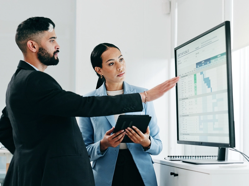 Two professionals discussing data on a large screen in an office.