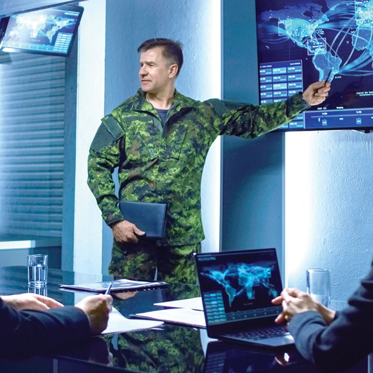 Military personnel discussing strategy with digital maps on screens.